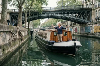 Bateau plat naviguant sur le canal Saint-Martin à Paris avec une guide en marinière près d'un pont en fer forgé